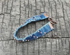 This blue denim bracelet is made from a pair of recycled blue jeans.   There are pink/salmon colored glass seed beads sewn onto the denim with a sturdy nylon thread.  These pink glass seed beads are a great touch to denim!   The toggle clasp and connections are copper colored metal. This blue denim bracelet is very comfortable.  It doesn't pinch or hurt your arm when you rest your arm against a hard surface, like many bracelets do. The measurement of this blue jeans bracelet is 7  1/4 inches (th Handmade Blue Denim Jewelry, Rustic Handmade Blue Beaded Bracelets, Denim Bracelets, Fabric Bracelets Diy, Denim Cuff Bracelet, Jeans Recycling, Beaded Denim, Recycled Bracelets, Denim Bracelet