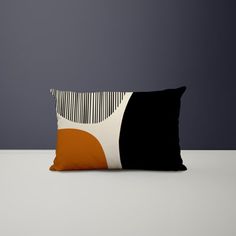 an orange and black pillow sitting on top of a white table next to a gray wall