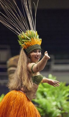 a woman in an orange skirt and headdress is dancing with feathers on her head