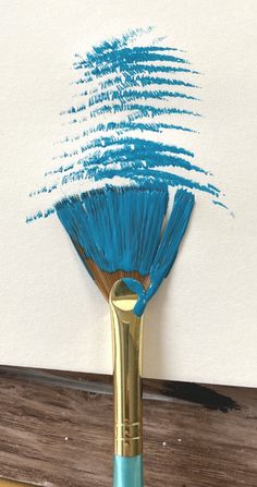 a brush with blue paint on it sitting on top of a wooden table next to a white wall