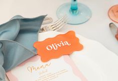 an orange and white place setting with blue napkins, silverware and utensils