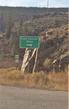 a highway sign on the side of a road in front of a hill and trees