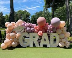 a large balloon sign that says grad with balloons all over the letters and trees in the background