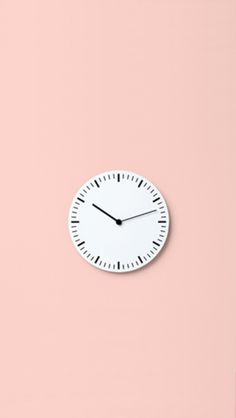 a white clock sitting on top of a pink wall