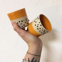 two coffee cups with black dots on them are held up in the air by a woman's hand