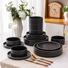 a table topped with black plates and silverware next to a vase filled with flowers