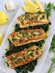 three pieces of fish on top of greens and lemons