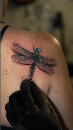 a dragonfly tattoo on the back of a woman's upper arm and shoulder