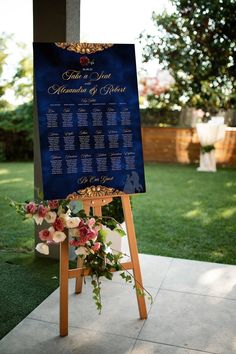 a blue and gold wedding seating sign with flowers on the front, along with an easel