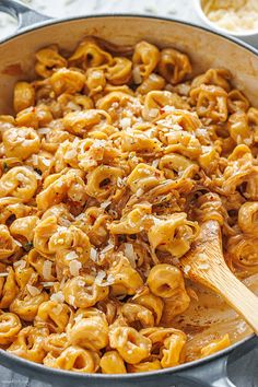 a pan filled with macaroni and cheese being stirred by a wooden spatula