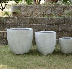 three cement planters sitting next to each other on the grass in front of a brick wall