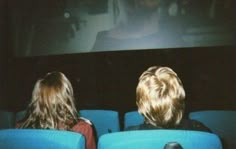 two children sitting in blue chairs watching a movie