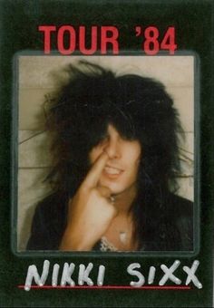 an old photo of a woman with long hair and piercings on her face, in front of a white brick wall