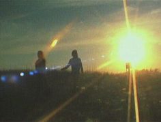 two people standing on train tracks with the sun setting in the back ground behind them