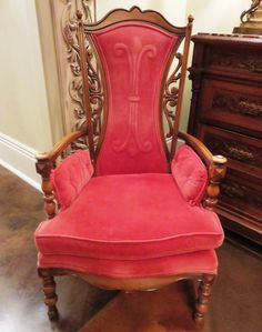 a red chair sitting on top of a wooden floor next to a dresser and mirror