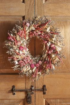 a wreath hanging on the front door of a house with dry grass and flowers in it