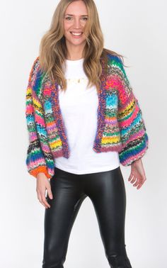 a woman wearing black leather pants and a multicolored cardigan sweater is standing in front of a white background