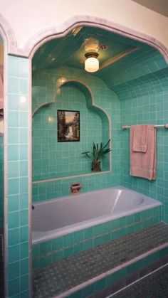 a bathroom with green tiles and a white bathtub next to a mirror on the wall