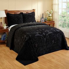 a bed with black bedspread and pillows in a room next to a window