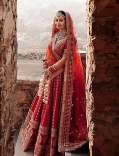 a woman in an orange and red bridal outfit standing on a ledge looking out at the city