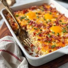 a casserole dish with eggs and bacon in it on a cutting board next to a fork