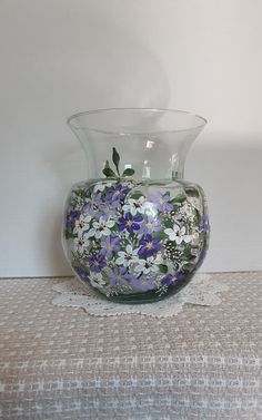 a glass vase with purple and white flowers painted on the inside is sitting on a table