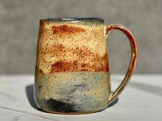 a brown and black coffee mug sitting on top of a white countertop next to a gray wall