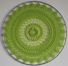 a green crocheted doily is shown on a white wall with a circular design in the center