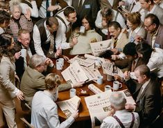 a large group of people gathered around a table with coffee mugs and papers on it