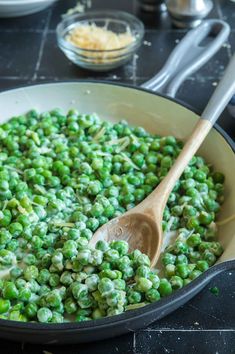 peas being cooked in a skillet with a wooden spoon on the side and other dishes to the side