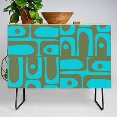 a blue and green cabinet sitting next to a potted plant on top of a metal stand