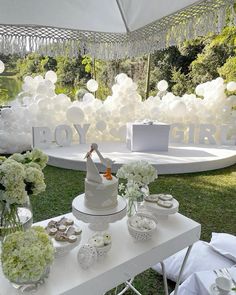 a white table topped with cake and cupcakes under a canopy covered in balloons