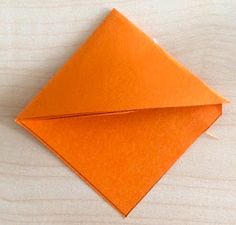 an orange origami envelope sitting on top of a wooden table next to a piece of paper