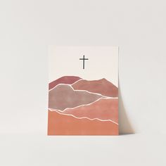 a card with a cross on top of it and mountains in the background, against a white wall