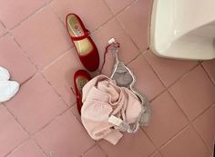 a pair of red shoes sitting on top of a pink floor next to a white sink