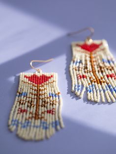 Hand beaded cream colored fringe earrings with red and blue vintage flower motif, close up. Beige Bohemian Fringe Earrings, Traditional Brown Handwoven Beaded Earrings, Traditional Beaded Fringe Earrings For Summer, Bohemian Cream Dangle Earrings, Traditional Beaded Beige Jewelry, Bohemian Beige Beaded Earrings For Gifts, Beige Bohemian Jewelry With Fringe, Bohemian Beige Fringe Jewelry, Traditional Fringe Earrings