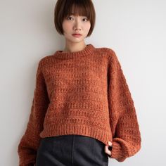 a woman wearing an orange sweater standing next to a white wall