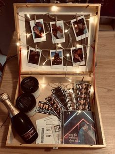 an open suitcase with pictures and other items in it sitting on a wooden table next to a bottle of wine