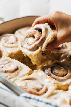 someone holding a piece of cinnamon rolls in a pan