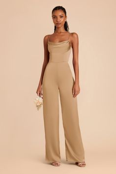 a woman in a tan jumpsuit holding a white bouquet and posing for the camera