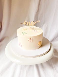 a white cake sitting on top of a plate with a one sign on top of it