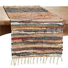 a multicolored table runner with tassels and fringe on it, sitting on top of a wooden table