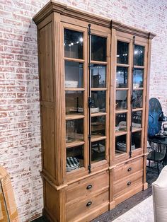 a large wooden china cabinet with glass doors and drawers in a room next to a brick wall