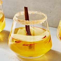 an apple cider with cinnamon sticks in it next to two glasses filled with liquid