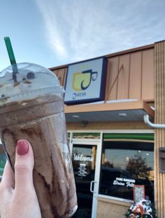 a person holding up a drink in front of a building