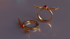 two gold rings with dragon wings on them, one has a red stone in the middle