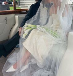 a bride and groom sitting in the back seat of a car with veil over their heads