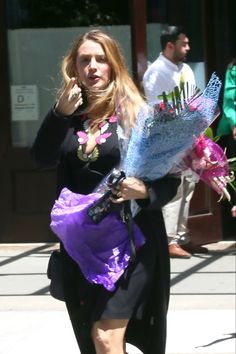 a woman is walking down the street with flowers in her hand and talking on the phone