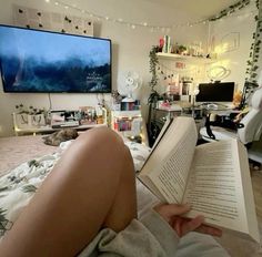 a person laying on a bed reading a book in front of a flat screen tv