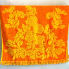 an orange and yellow flowered blanket hanging on a wall with tassels around it